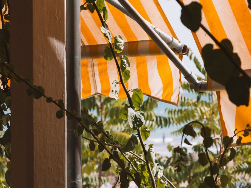 Tenda da sole a bracci a righe bianche e arancioni tra piante rampicanti
