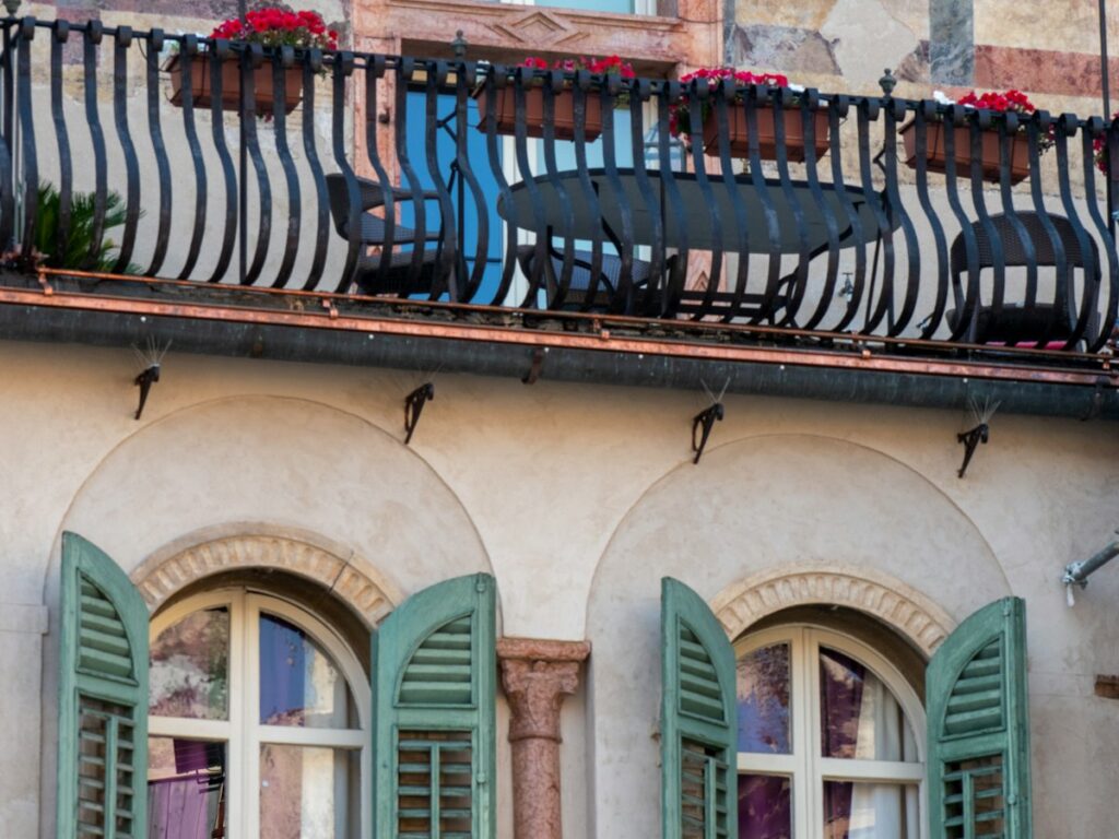 Balcone fiorito con persiane verdi a lamelle su una facciata storica in una città italiana